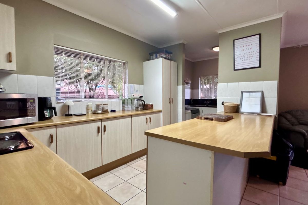 A functional kitchen featuring laminate countertops, built-in cabinetry, tiled splashbacks, and a central island, with an adjacent scullery area visible.