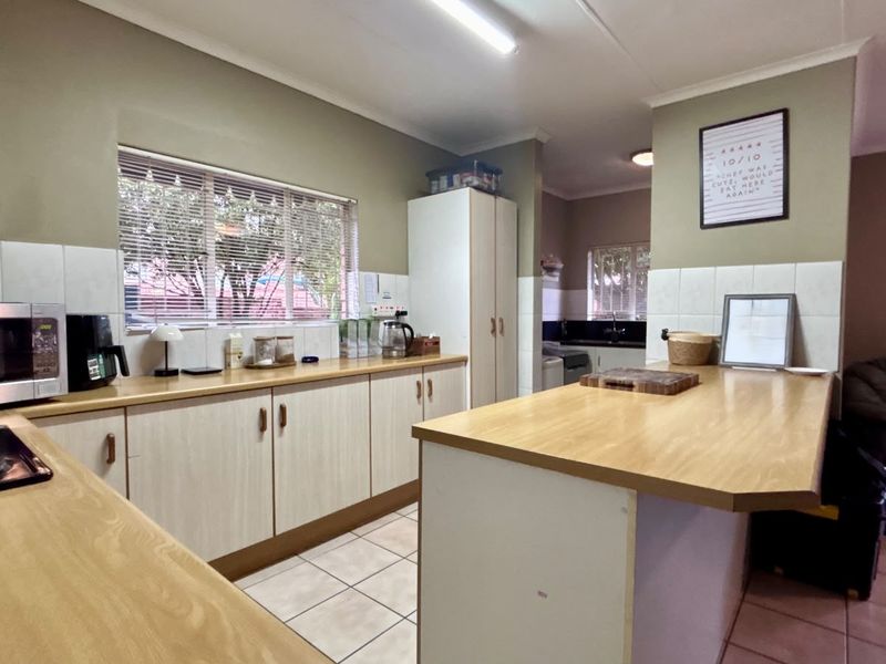 A functional kitchen featuring laminate countertops, built-in cabinetry, tiled splashbacks, and a central island, with an adjacent scullery area visible.