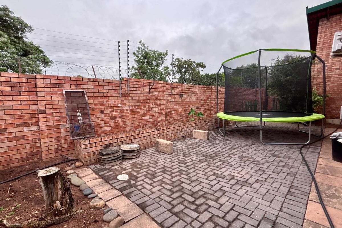 A rear outdoor area featuring a paved patio, brick boundary wall with electric fencing, and an external wall light.