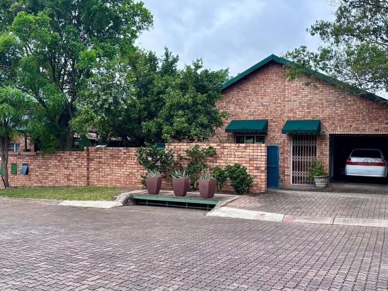 Front view of a face brick house featuring a paved driveway, integrated garage, and secure boundary wall with green metal gates.