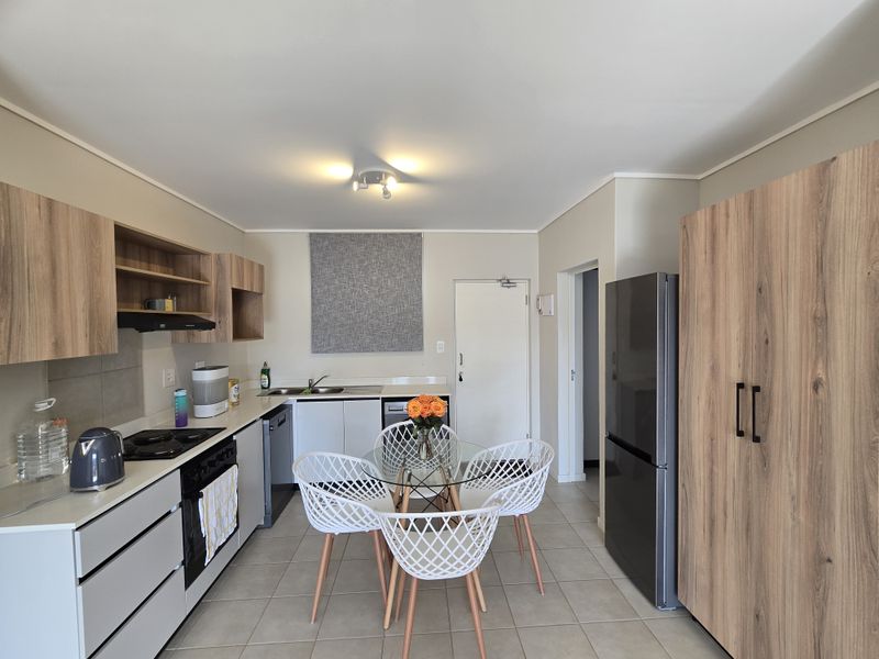 Modern kitchen featuring wood-look cabinetry, integrated appliances, tiled flooring, and a functional layout with ample storage and a dedicated dining area.