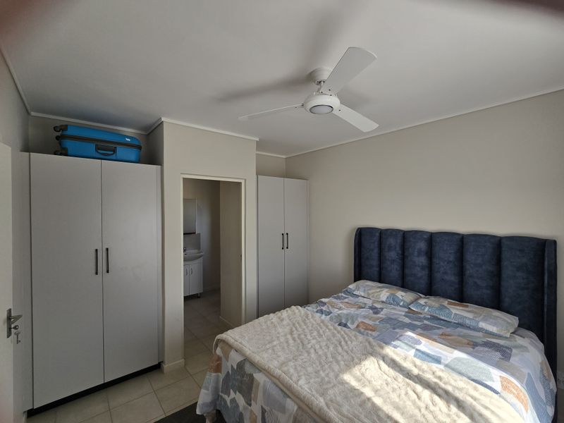 A well-maintained bedroom featuring built-in cupboards, a ceiling fan, and tiled flooring, with an adjoining en-suite bathroom visible.