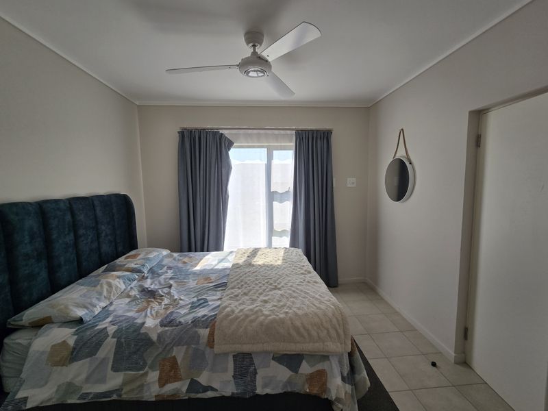 A well-lit bedroom featuring neutral walls, tiled flooring, a ceiling fan, and a sliding door providing access to the exterior.