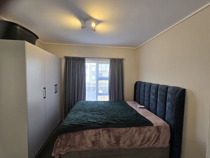 A well-maintained bedroom featuring a built-in wardrobe, neutral wall finishes, and a window with curtain treatments.