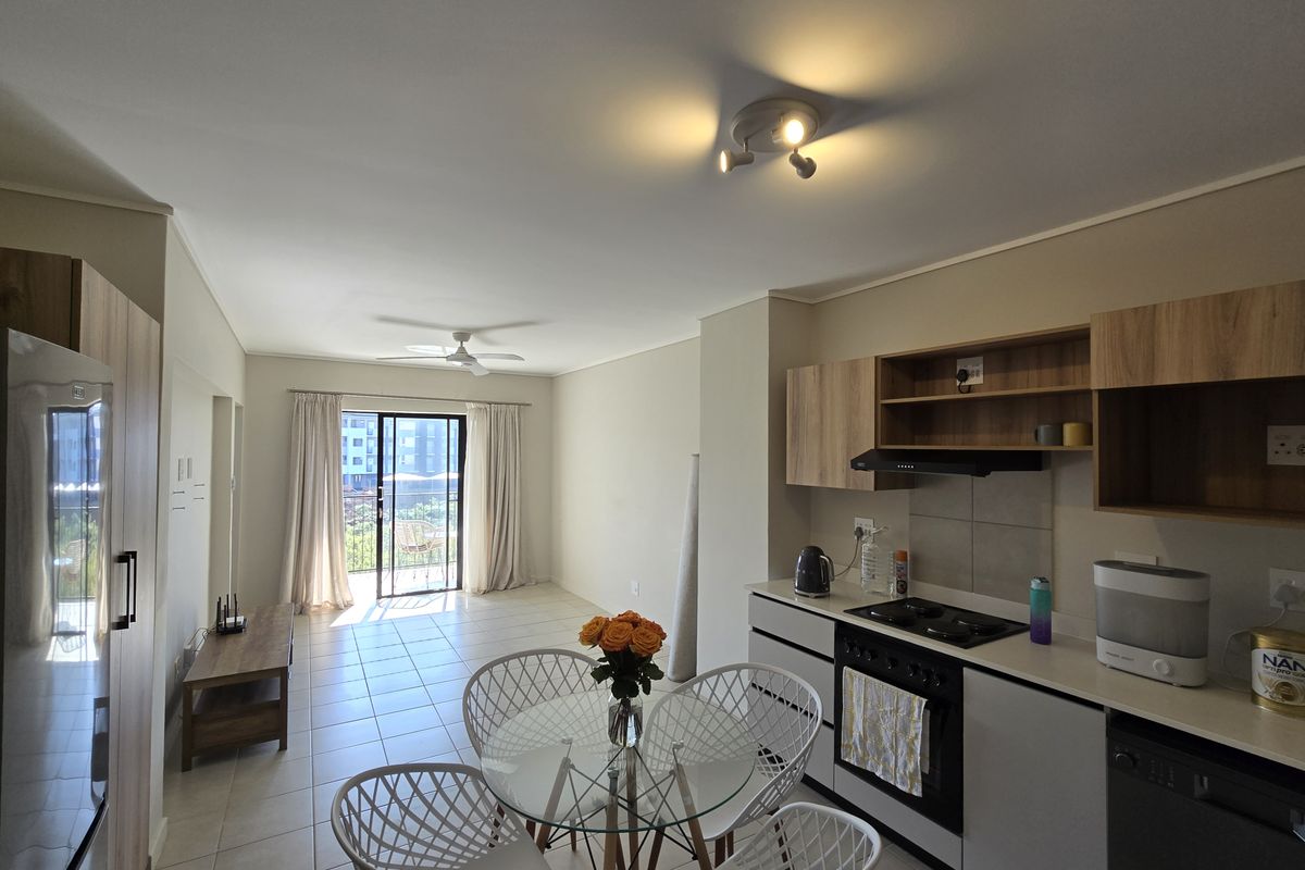 Open-plan living and kitchen area featuring modern cabinetry, built-in appliances, tiled flooring, and a sliding door leading to a balcony.