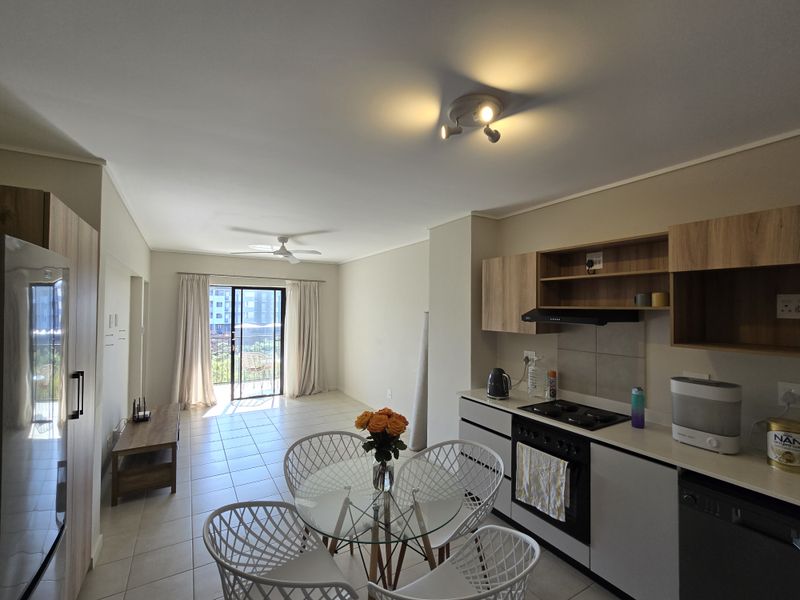 Open-plan living and kitchen area featuring modern cabinetry, built-in appliances, tiled flooring, and a sliding door leading to a balcony.