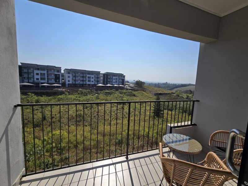 A covered balcony featuring tiled flooring and a metal balustrade, offering an open view of the surrounding landscape and neighboring apartment buildings.