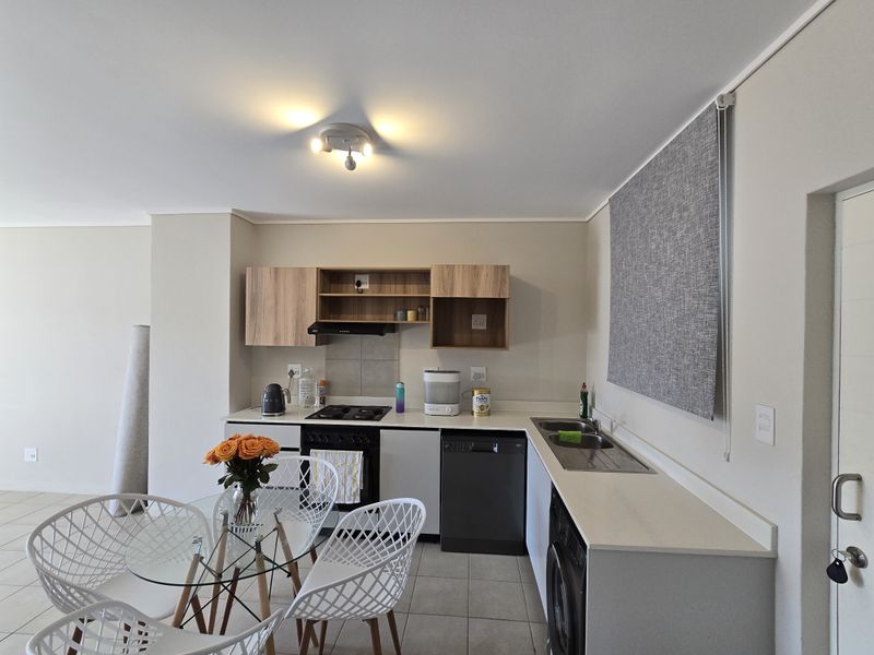 Modern kitchen featuring light wood-tone cabinetry, built-in oven and hob, double sink, and tiled flooring, offering a clean and functional workspace.