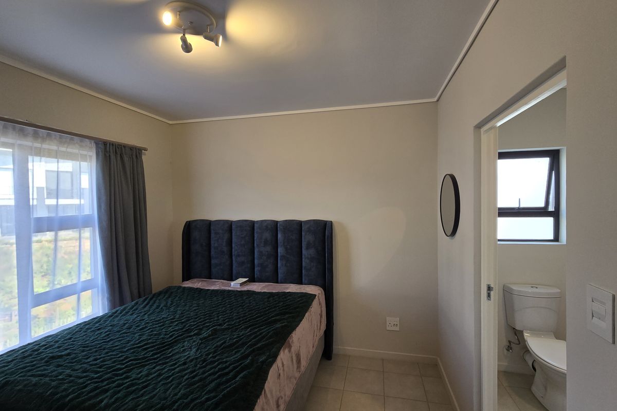 A well-maintained bedroom featuring tiled flooring, neutral wall finishes, and direct access to an en-suite bathroom with a toilet.
