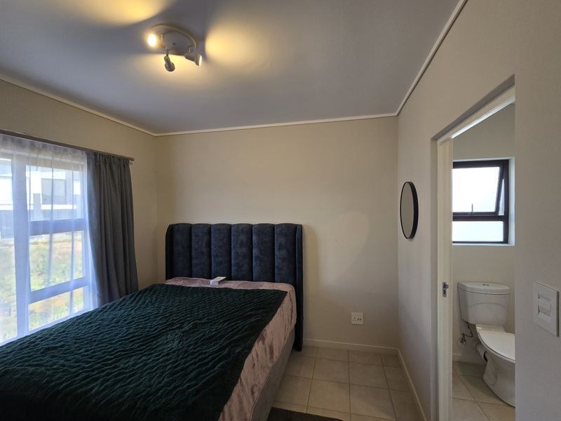 A well-maintained bedroom featuring tiled flooring, neutral wall finishes, and direct access to an en-suite bathroom with a toilet.