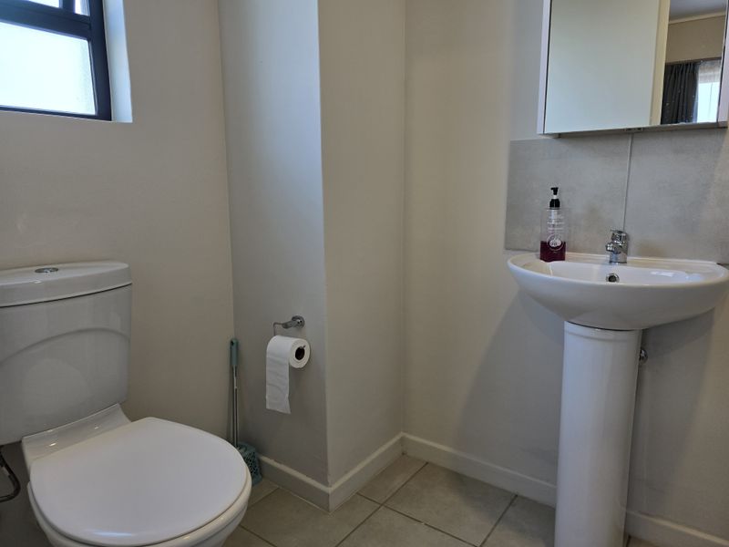 A clean and functional bathroom featuring a pedestal basin, wall-mounted mirror cabinet, and standard toilet with tiled flooring.