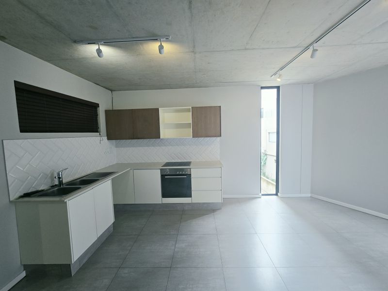 Modern open-plan kitchen featuring sleek cabinetry, integrated appliances, herringbone backsplash, and exposed concrete ceilings, creating a contemporary and minimalist living space.