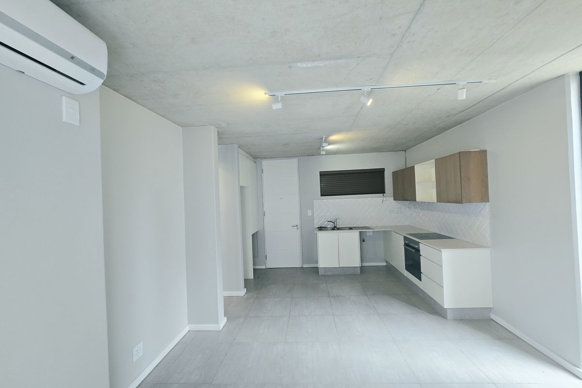 Modern open-plan living area featuring an exposed concrete ceiling, tiled floors, and a sleek kitchen with built-in appliances and contemporary cabinetry.