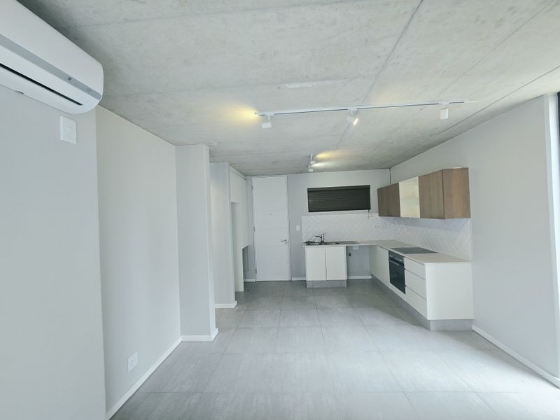 Modern open-plan living area featuring an exposed concrete ceiling, tiled floors, and a sleek kitchen with built-in appliances and contemporary cabinetry.