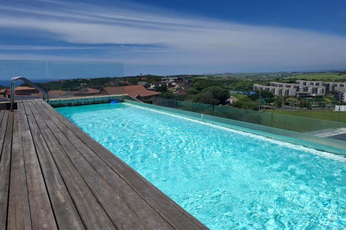 An elevated infinity edge swimming pool featuring timber decking and a glass balustrade, offering expansive views of the surrounding landscape.