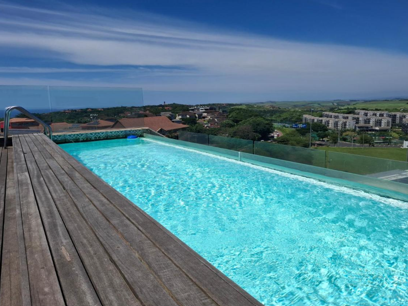 An elevated infinity edge swimming pool featuring timber decking and a glass balustrade, offering expansive views of the surrounding landscape.