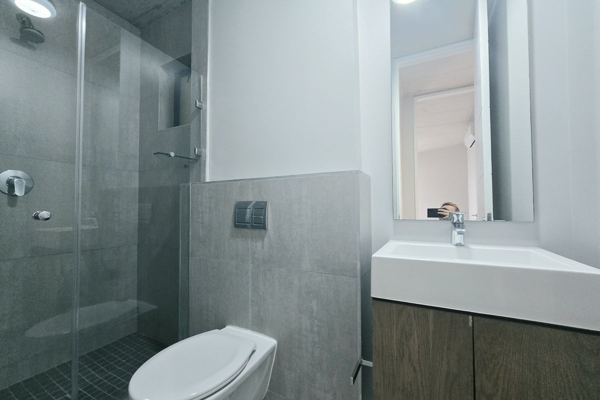 Modern bathroom featuring a walk-in shower with glass screen, wall-mounted toilet, and a vanity unit with basin and mirror.