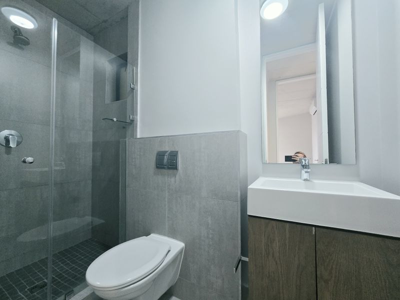 Modern bathroom featuring a walk-in shower with glass screen, wall-mounted toilet, and a vanity unit with basin and mirror.