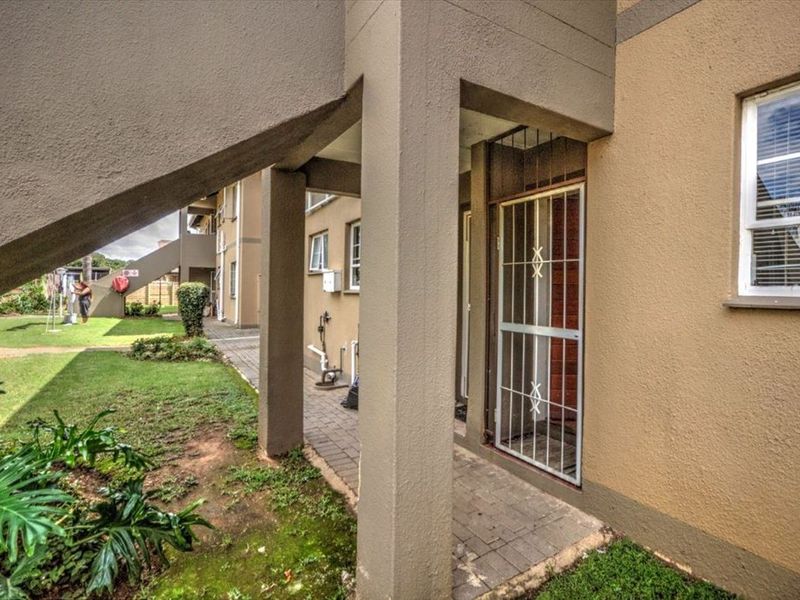 Rear exterior view of the apartment building featuring a paved walkway, security gate, and access to communal garden areas.
