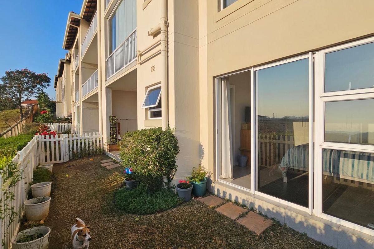 Rear view of the apartment building featuring a private garden area, white picket fencing, and sliding glass doors providing access to the interior.