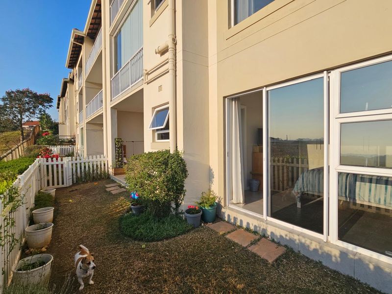 Rear view of the apartment building featuring a private garden area, white picket fencing, and sliding glass doors providing access to the interior.
