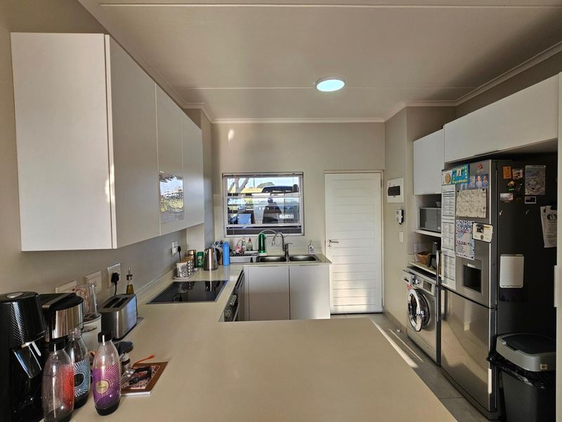 A modern, well-maintained kitchen featuring white cabinetry, stone countertops, integrated appliances, and a functional layout with a dedicated laundry area.
