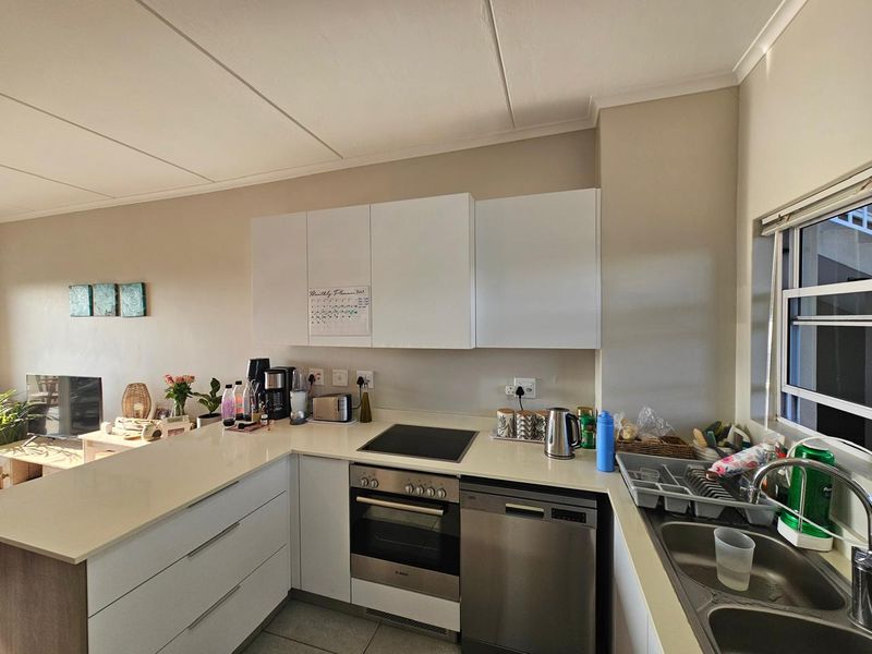 Modern kitchen featuring white cabinetry, stone countertops, built-in oven, electric hob, and a stainless steel dishwasher with a double bowl sink.