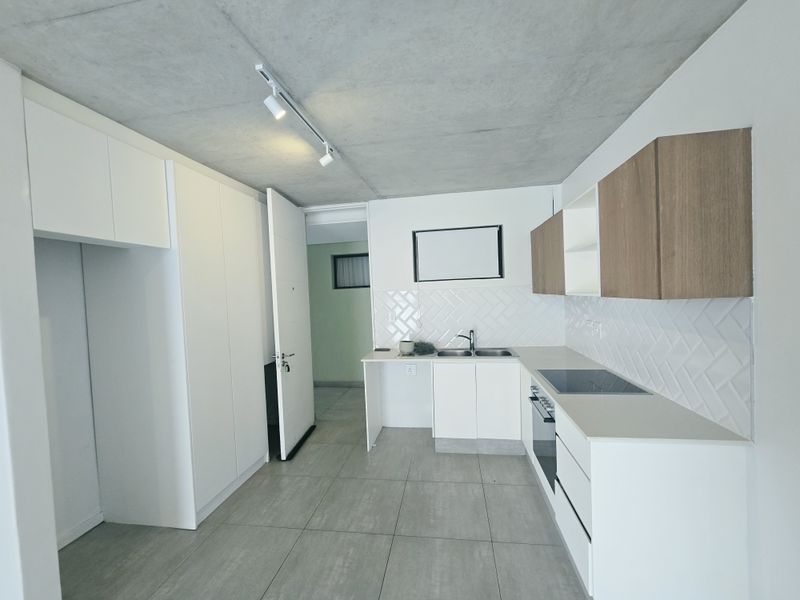 Modern kitchen featuring sleek white and wood-tone cabinetry, herringbone tile backsplash, integrated appliances, and an exposed concrete ceiling with track lighting.