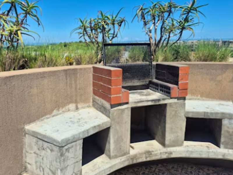 Outdoor patio area featuring a built-in brick braai, curved concrete bench seating, and decorative floor tiles with scenic landscape views.