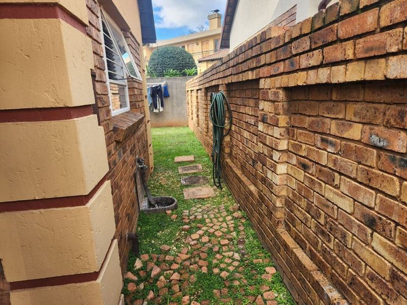 A narrow side passage featuring a brick boundary wall, external water tap, and paved walkway with integrated garden space.