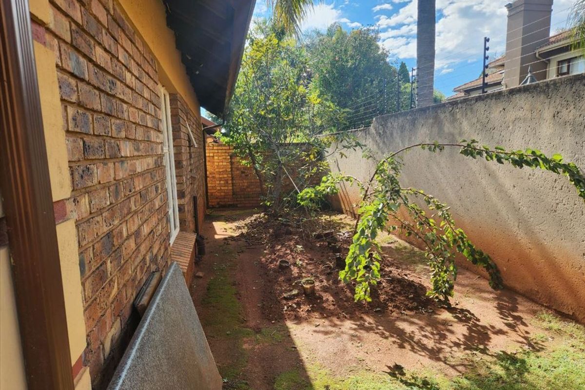 A side garden area featuring face brick exterior walls, a high boundary wall with electric fencing, and an unlandscaped soil ground surface.