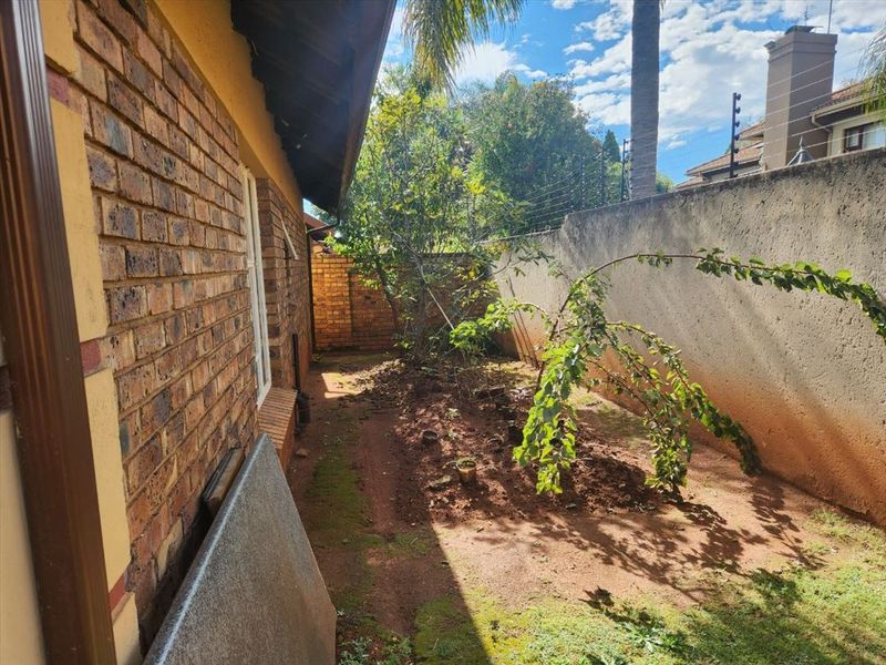 A side garden area featuring face brick exterior walls, a high boundary wall with electric fencing, and an unlandscaped soil ground surface.