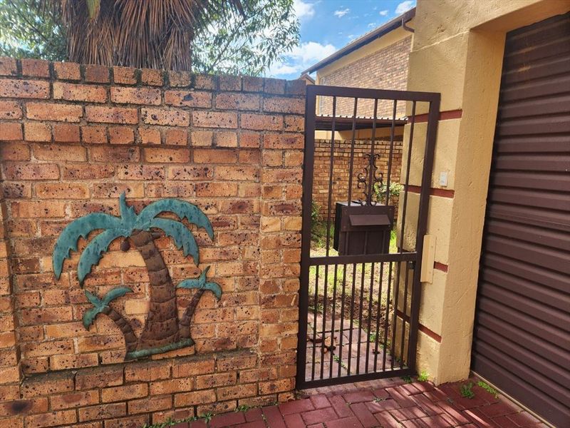 Front entrance area featuring a face brick boundary wall, metal pedestrian gate with integrated mailbox, and access to the garage.