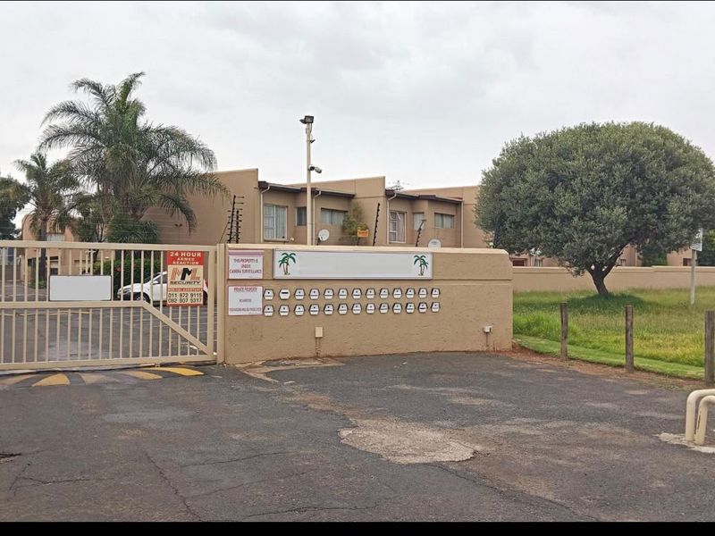 Front entrance view of the townhouse complex featuring a sliding security gate, perimeter wall with post boxes, and electric fencing.