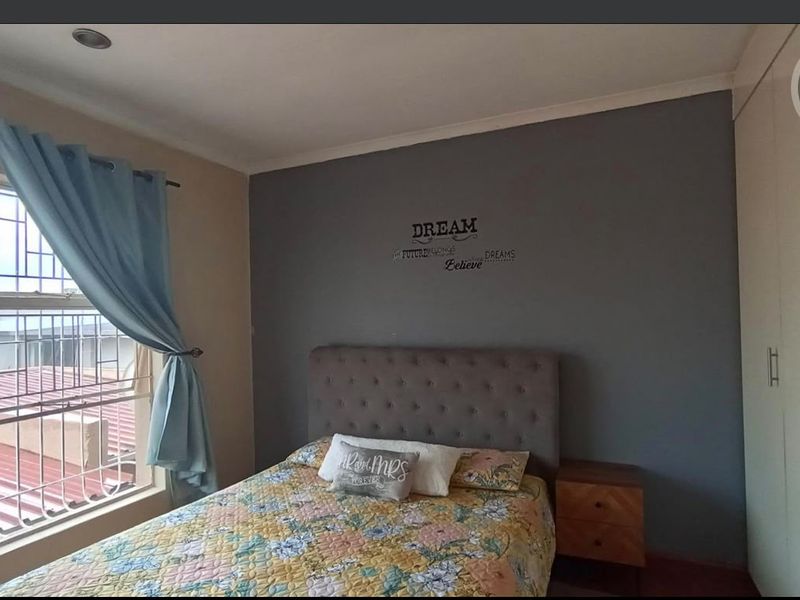 A bedroom featuring built-in cupboards, security bars on the window, and a neutral color scheme with a feature wall.