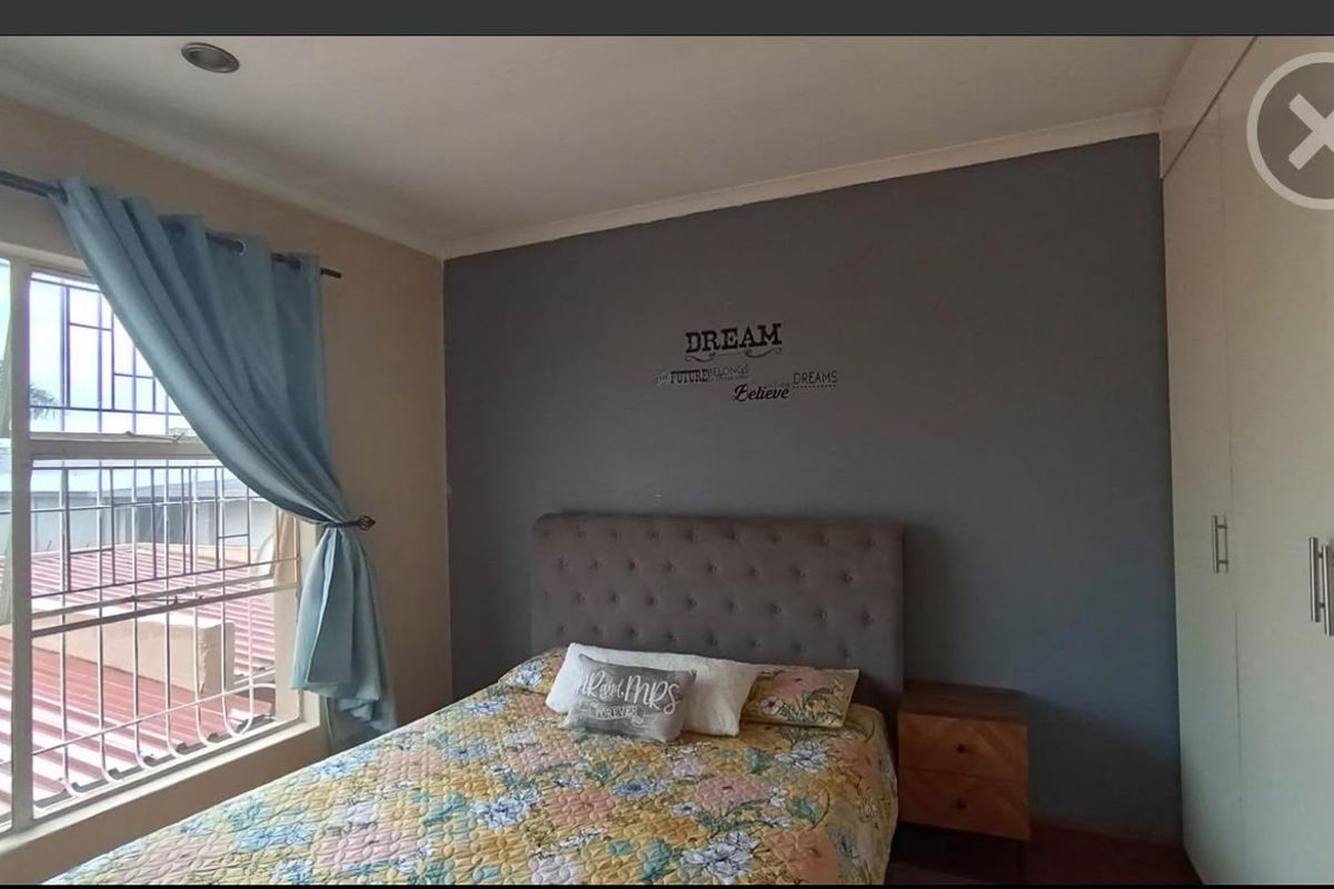 A bedroom featuring built-in cupboards, security bars on the window, and a neutral color scheme with a feature wall.