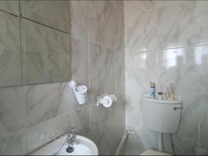 A compact bathroom featuring marble-look wall tiles, a ceramic washbasin with chrome faucet, and a standard toilet cistern.