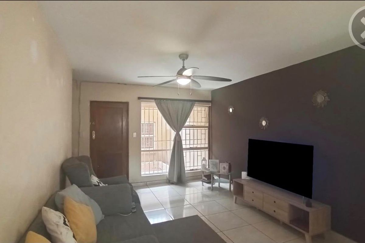 A living room featuring tiled flooring, a ceiling fan, and a window fitted with security bars.