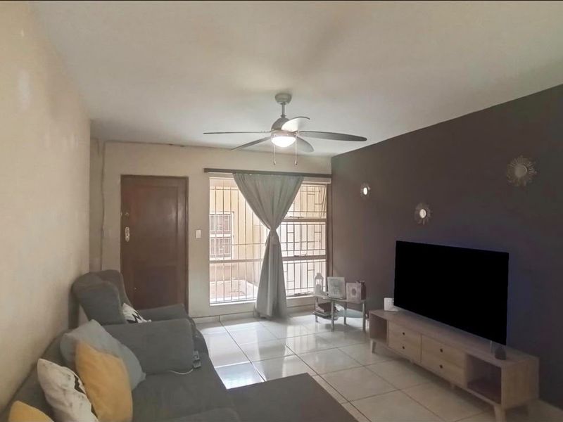 A living room featuring tiled flooring, a ceiling fan, and a window fitted with security bars.