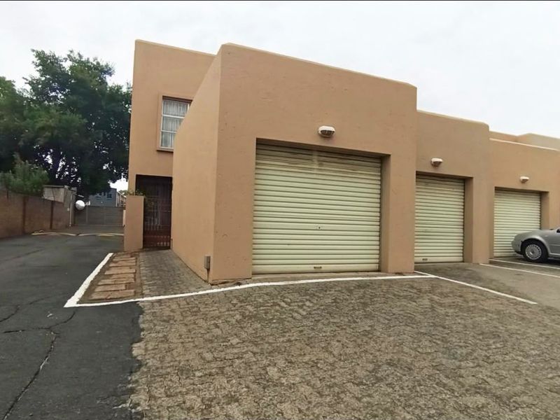 Front exterior view of a townhouse complex featuring multiple roller shutter garage doors and a paved driveway area.