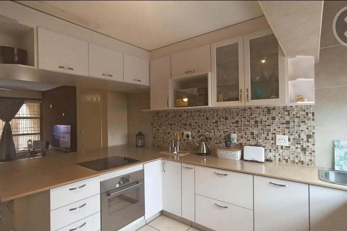 A functional kitchen featuring white cabinetry, mosaic tile backsplash, integrated electric hob and oven, and ample laminate countertop workspace.