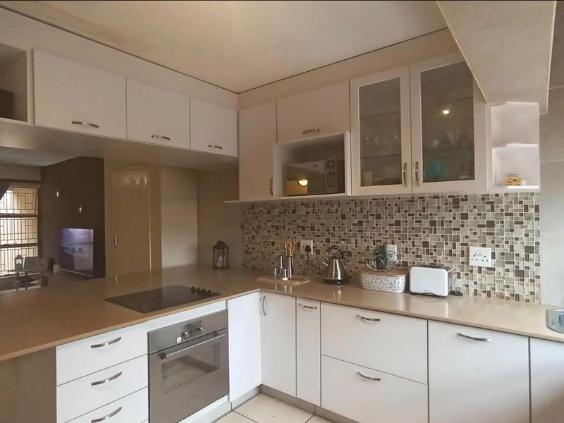A functional kitchen featuring white cabinetry, mosaic tile backsplash, integrated electric hob and oven, and ample laminate countertop workspace.
