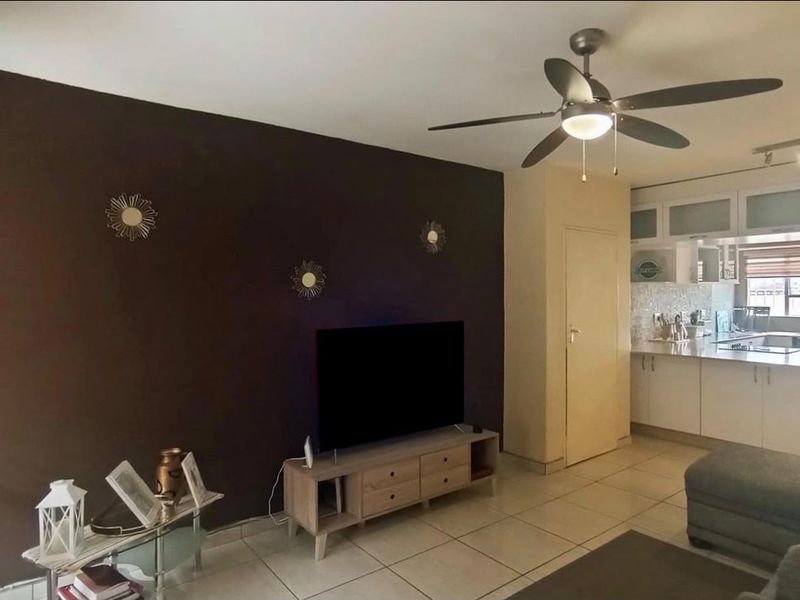 Open-plan living area featuring tiled floors, a ceiling fan, and an adjoining kitchen with white cabinetry and a breakfast counter.