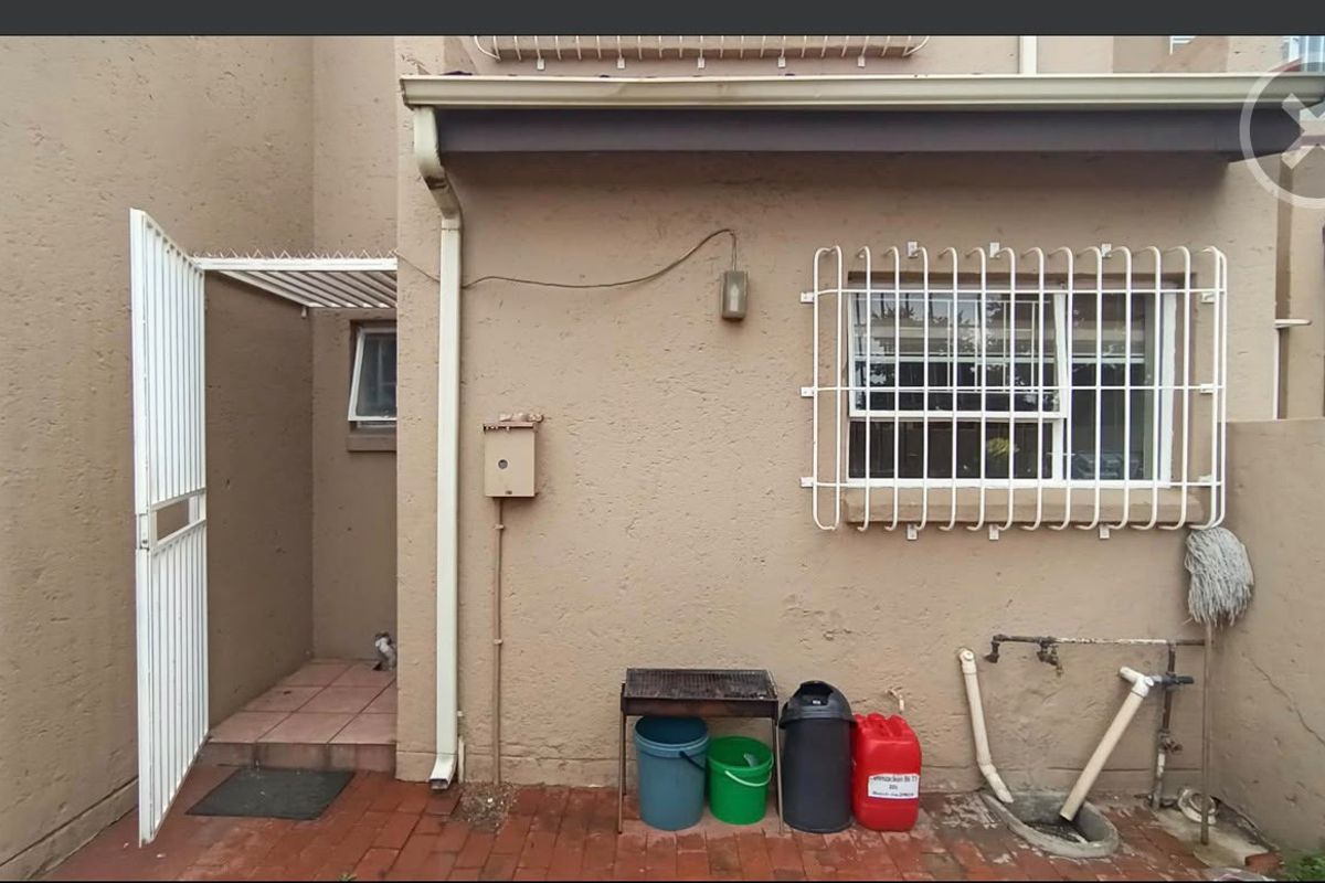 Rear exterior view of the townhouse featuring a paved courtyard, security gate, window security bars, and external plumbing fixtures.
