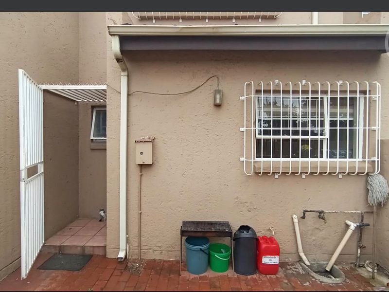 Rear exterior view of the townhouse featuring a paved courtyard, security gate, window security bars, and external plumbing fixtures.