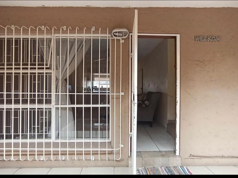 Front entrance of the townhouse featuring a tiled porch, security gate, and protective window bars, showing signs of exterior wear.