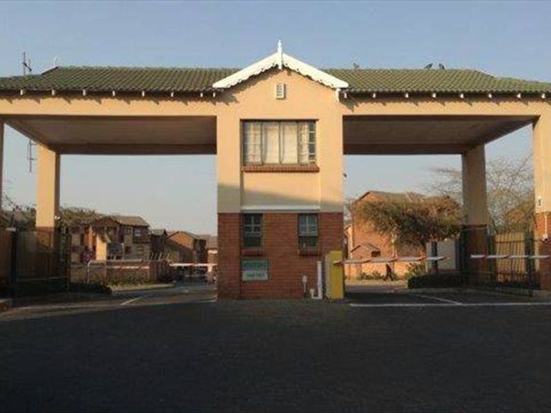 A view of the secure gated entrance and guardhouse for the apartment complex, featuring a boom gate and brick facade.