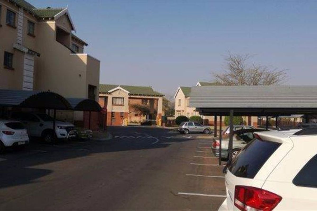 Exterior view of an apartment complex featuring covered parking bays and paved driveway access.