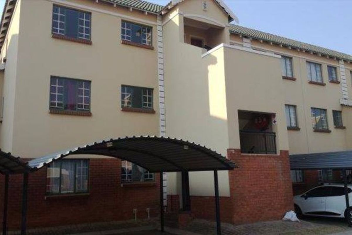 Exterior view of a multi-story apartment building featuring brick and plaster facade, tiled roofing, and covered carport parking bays.