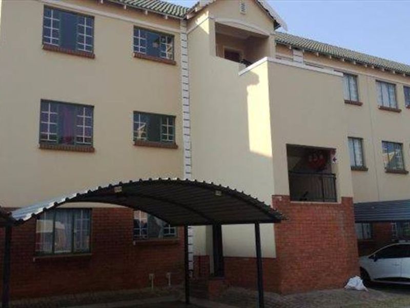 Exterior view of a multi-story apartment building featuring brick and plaster facade, tiled roofing, and covered carport parking bays.